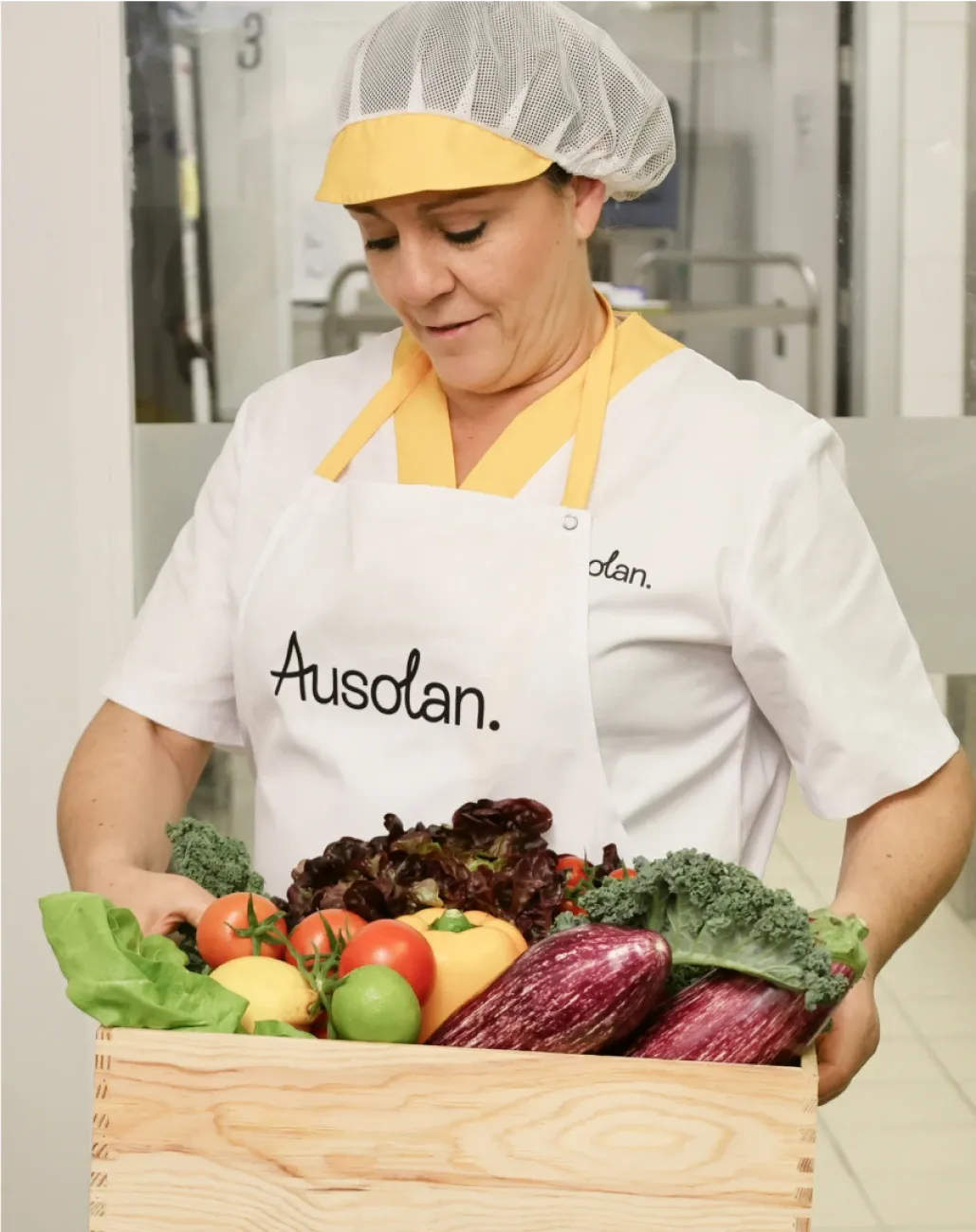Cocinera Ausolan con uniforme y caja de verduras frescas